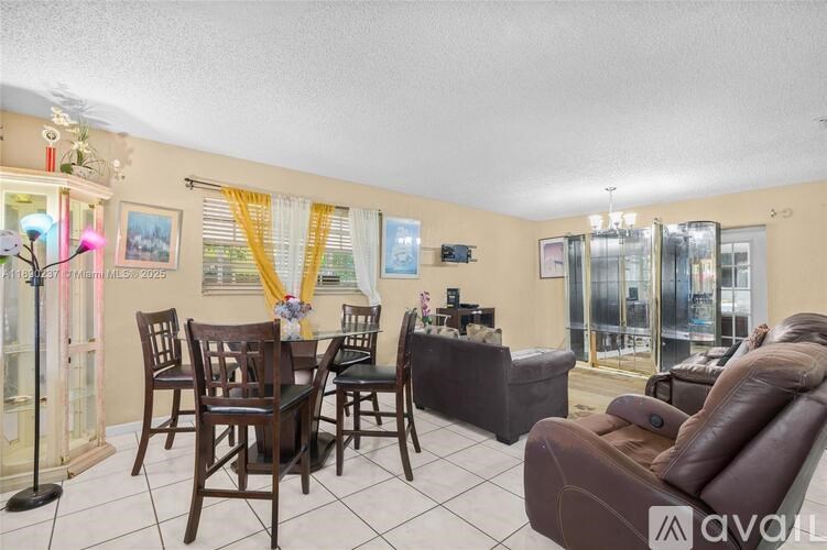 A living room with a brown leather couch, a wooden dining table with chairs, and a television mounted on the wall.