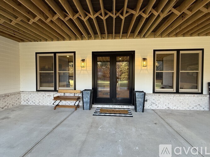 A wooden bench sits on a porch in front of a black door.