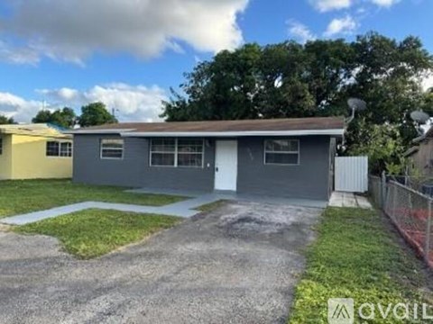 A grey building with a white door is surrounded by a grassy area and a fence.