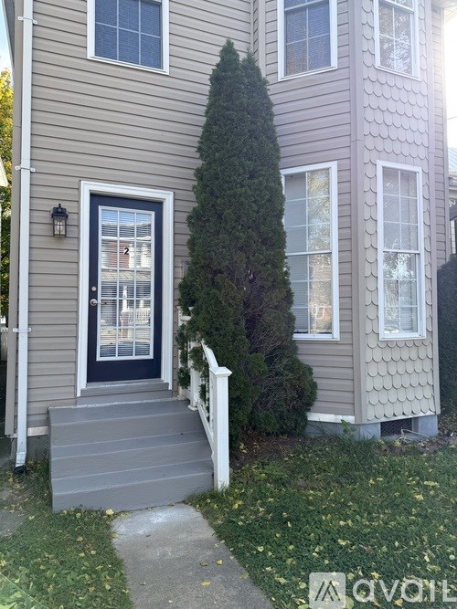 A grey house with a black door and a tree in front.