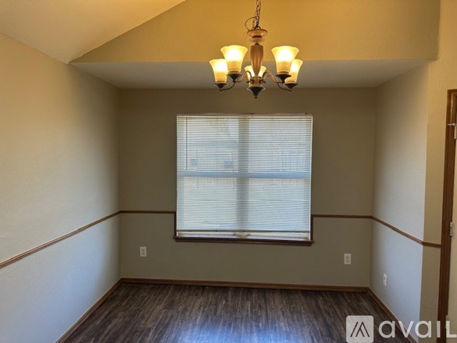 A room with a window covered by blinds and a chandelier hanging from the ceiling.