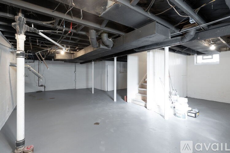 A large empty room with a concrete floor and white walls, with a staircase leading to another level.