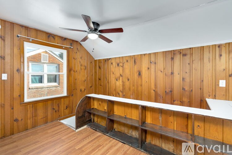A room with wooden walls and a window showing a house outside.