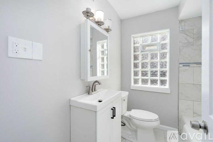 A white bathroom with a toilet, sink, mirror, and a window with a grid pattern.