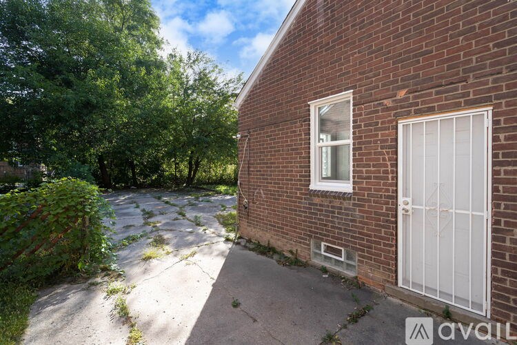 A brick building with a white door and window is surrounded by greenery.