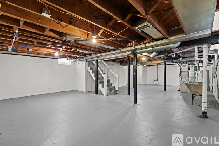 A spacious empty room with a staircase and a lot of pipes on the ceiling.