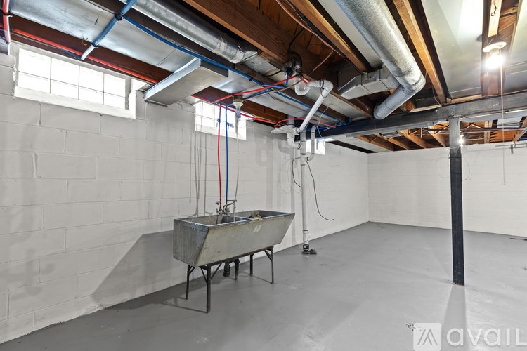 A room with a white floor and walls, a metal table, and a pipe running along the ceiling.