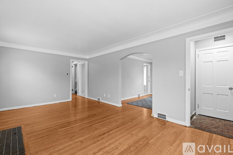 A room with wooden floors and white walls, with a door on the right and a window on the left.