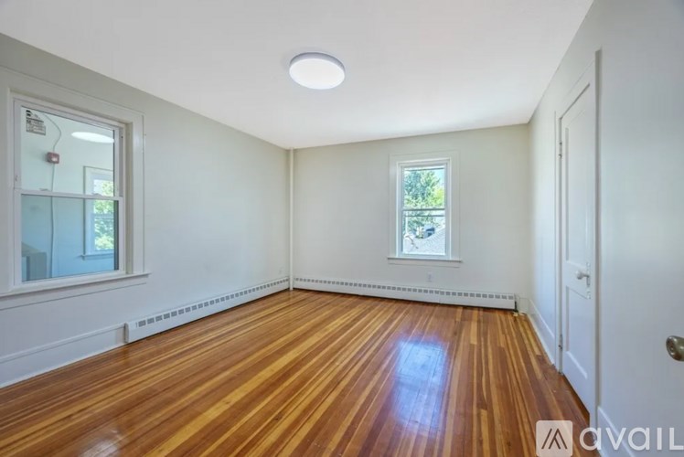 A room with wooden floors and white walls, with a window and a door visible.