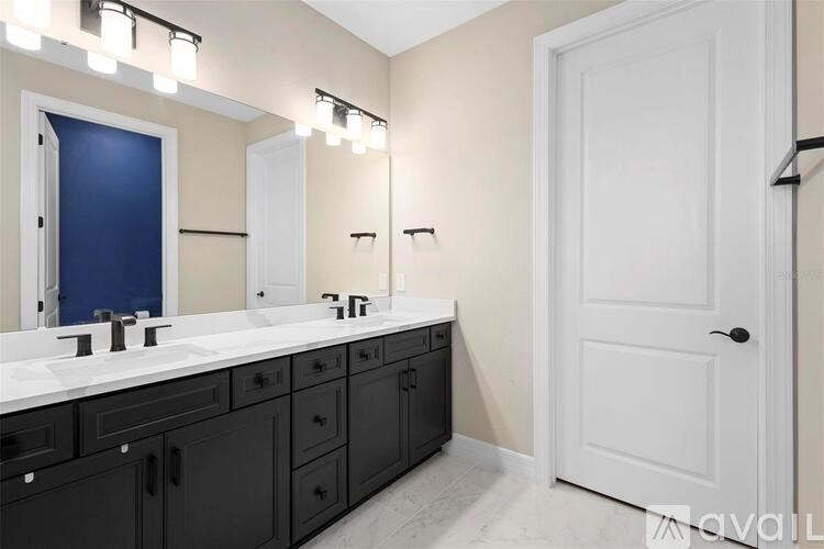 A bathroom with a white door, a vanity with a sink and a mirror above it.