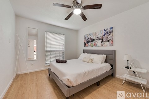 A bedroom with a bed, a ceiling fan, and a painting on the wall.