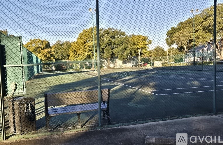 A tennis court is enclosed by a green fence.