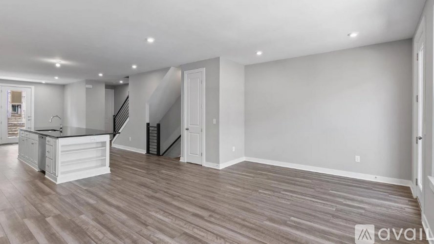 A spacious room with wooden flooring and a staircase in the background.