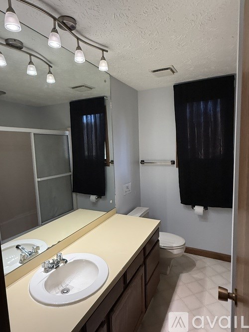 A bathroom with a sink, mirror, toilet and a towel rack.