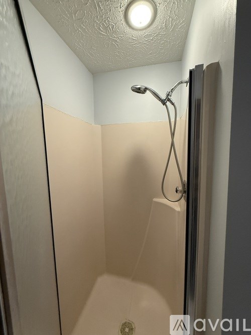 A small, white, square shower stall with a shower head and a light on the ceiling.