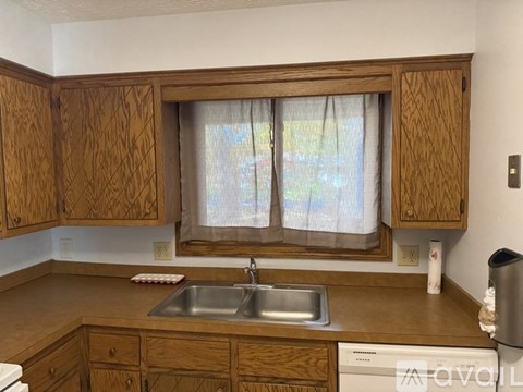 A kitchen with wooden cabinets and a window with curtains.
