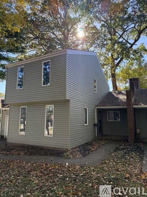 A house with a grey siding and a brown roof is surrounded by trees.