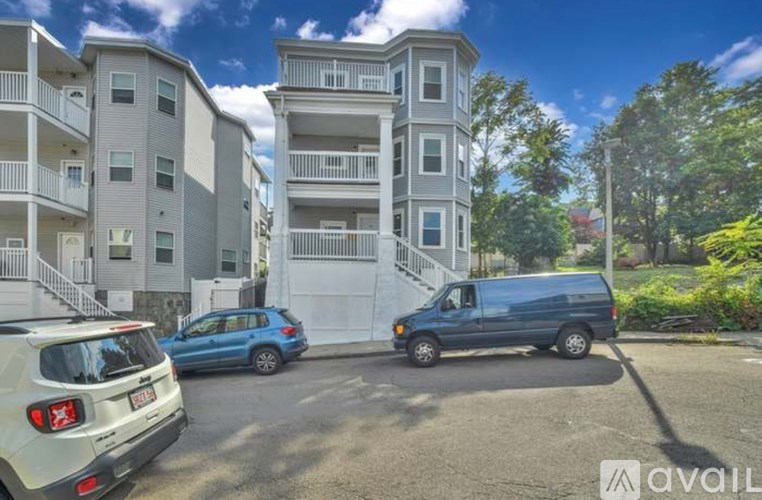 A white car is parked in front of a blue van and a white building.