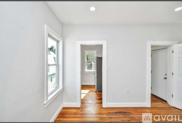 A room with white walls and wooden floors, with a window on the left and a door on the right.