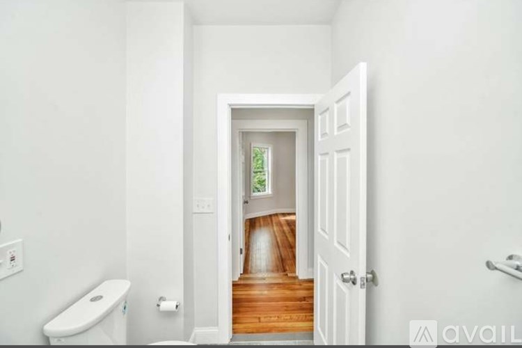 A white bathroom with a toilet and a doorway leading to a hallway.
