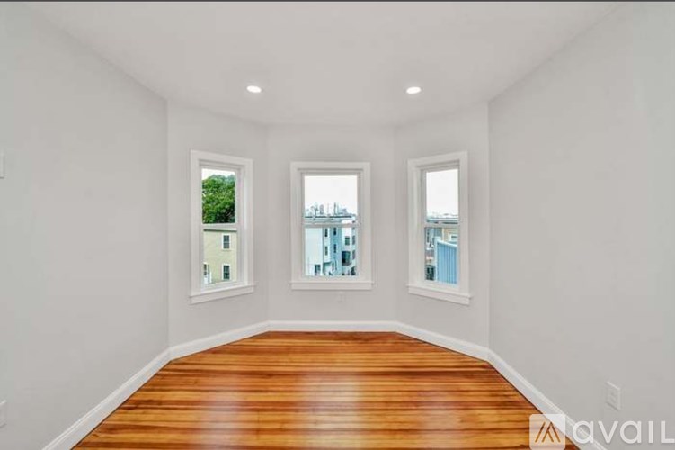 A room with wooden floors and white walls has two windows.