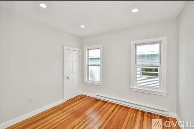 A room with wooden floors and two windows with blinds.