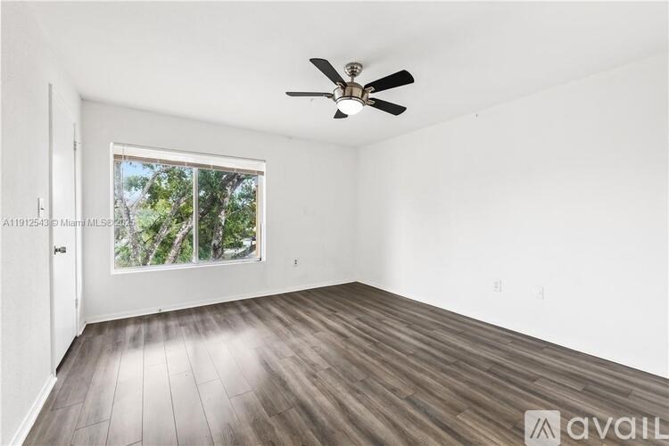 A room with a ceiling fan and a window showing trees outside.