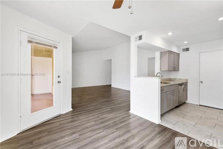 A spacious room with a kitchenette and a door leading to another room.