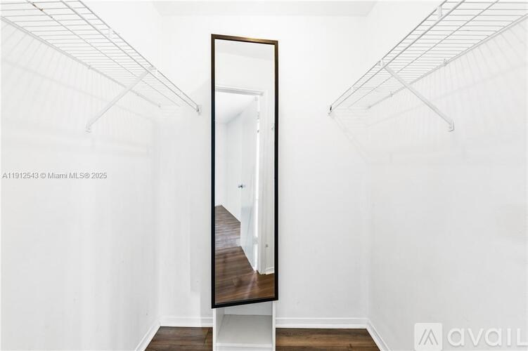 A large mirror in a white room with a wooden floor.