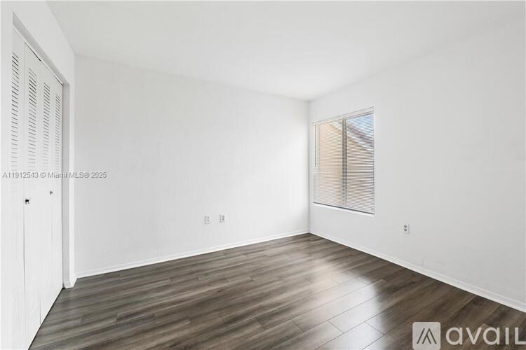 A room with wooden flooring and a window with blinds.
