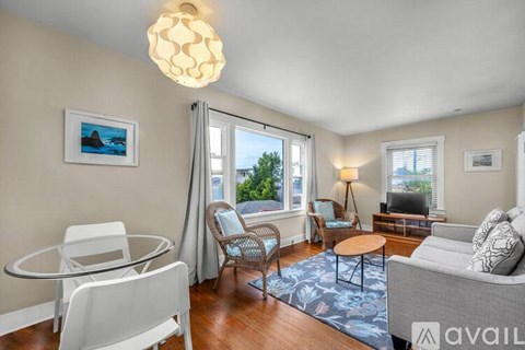 A living room with a grey couch, a glass table, and a painting on the wall.