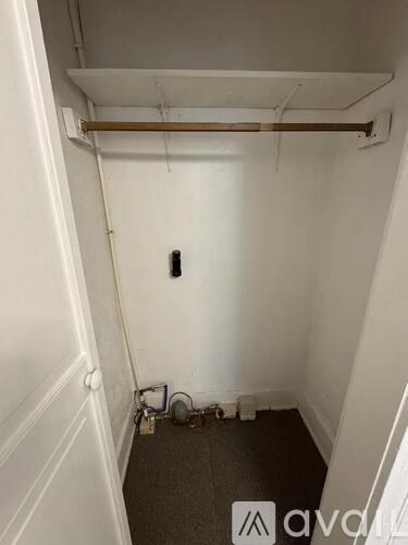 A small, untidy room with a white wall and a brown pipe running along the top.