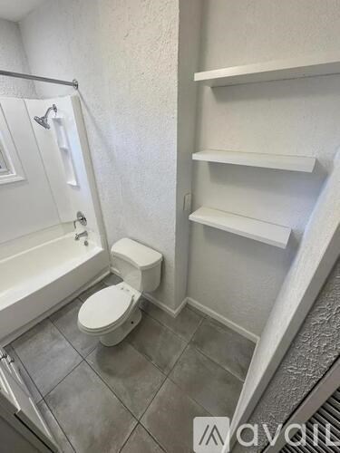 A white toilet in a small bathroom with a white bathtub and a white shelf.