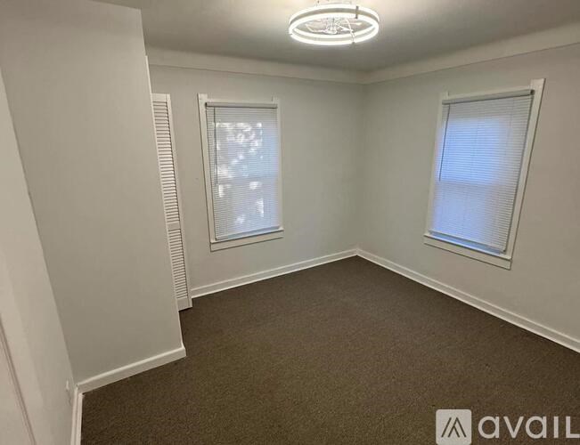 A room with carpeted floor, two windows with blinds, and a ceiling fan.