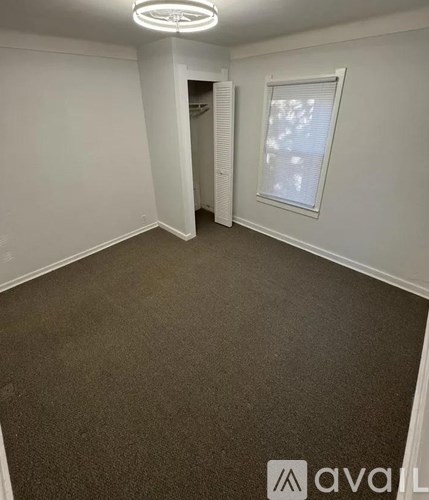 A carpeted room with a window and a door leading to another room.