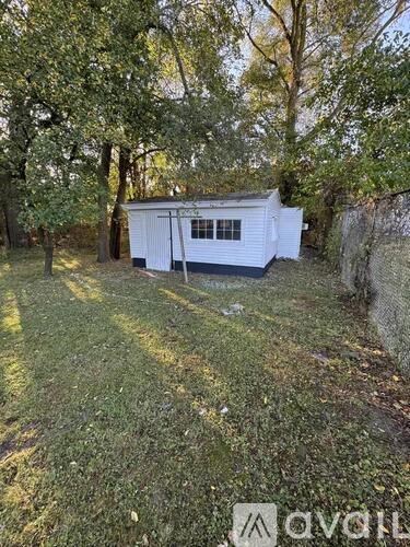A small white building with a window is surrounded by trees.