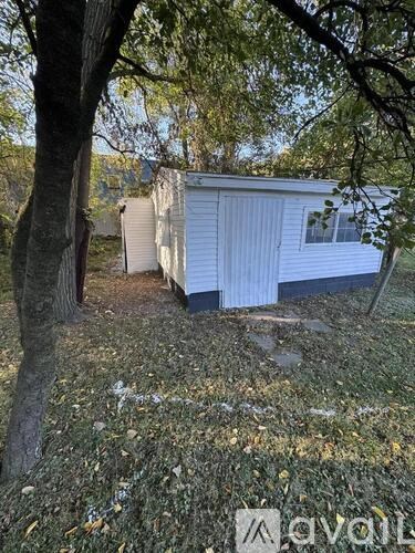 A white mobile home sits in a grassy area with trees around it.