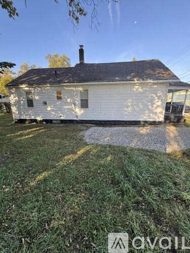 A white house with a black roof and a chimney is surrounded by grass.