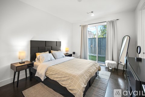 A bedroom with a large bed, a nightstand with a lamp, and a window with curtains.