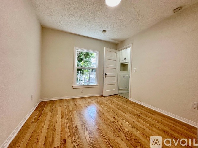 A room with wooden flooring and a window with a view of trees.