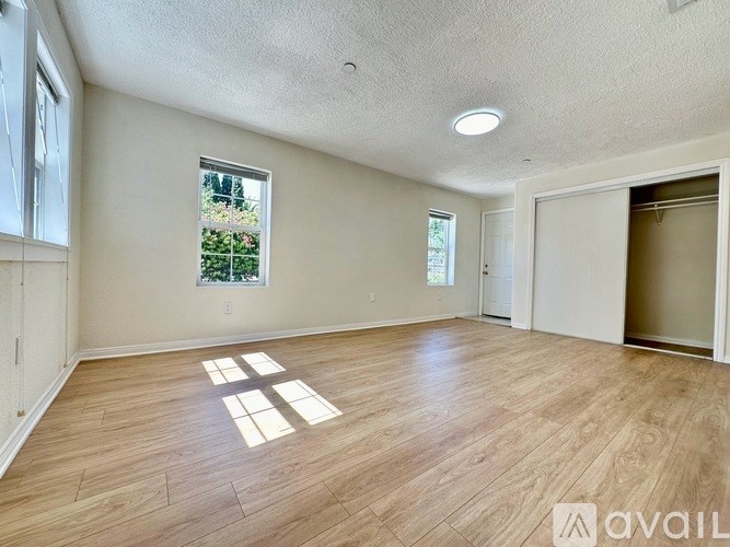 A room with wooden flooring and a window showing greenery outside.