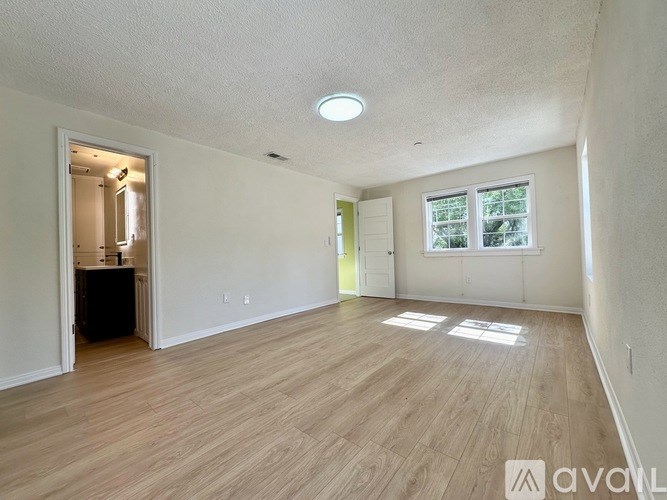 A room with wooden flooring and a window with sunlight coming through.
