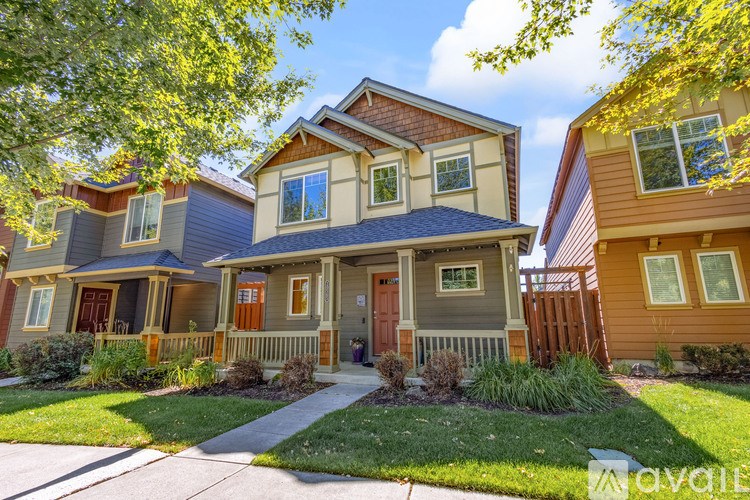 A house with a brown door and a grey roof is surrounded by greenery.