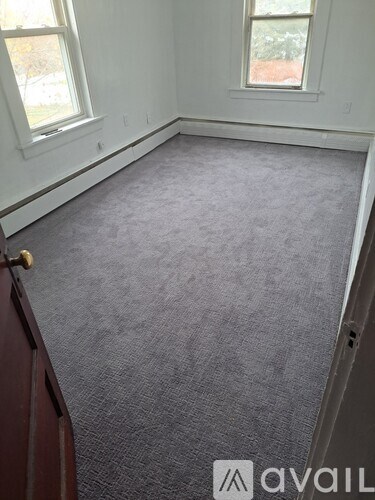 A room with a grey carpet and a window.