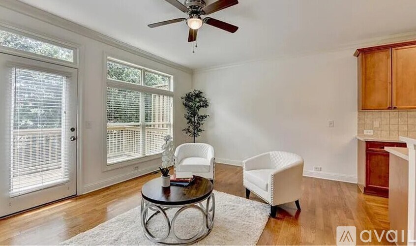 A living room with a ceiling fan, a table with a plant and a bottle on it, a chair, and a white sofa.