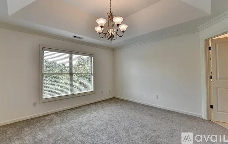 A room with a chandelier, a window with blinds, and a carpeted floor.