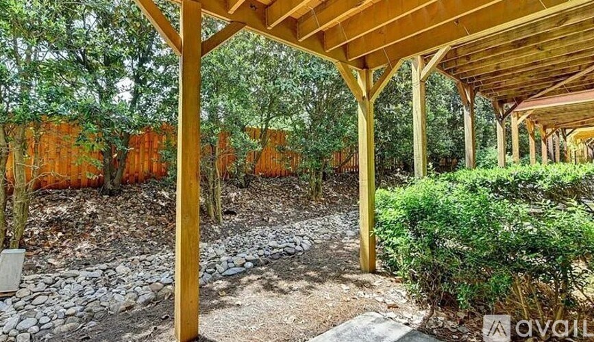A wooden pergola is situated in a garden with a gravel path and greenery.