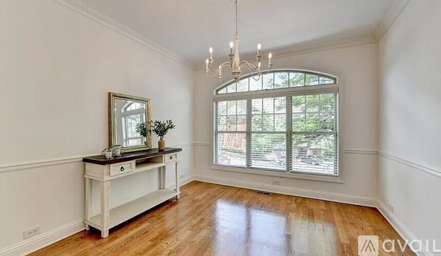 A room with a wooden floor, a white table with a mirror and flowers, and a chandelier.