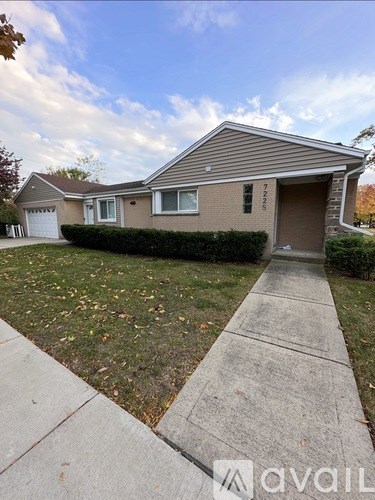 A house with a brown garage door and a white door is surrounded by a lawn and a sidewalk.