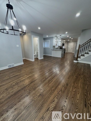A spacious room with wooden flooring and a chandelier hanging from the ceiling.